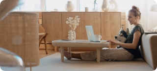 Woman sits on living room floor using laptop, accompanied by a Siberian Husky.